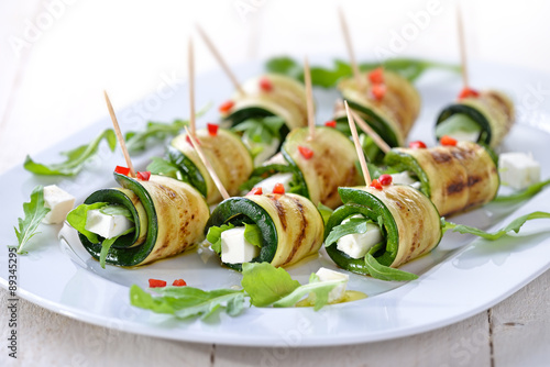 Gebratene Zucchiniröllchen mit Feta und Rucola, mit Olivenöl und Paprika serviert