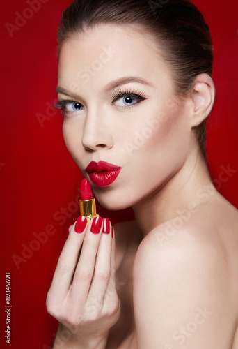 Beautiful woman with red lips holding a lipstick. isolated on red background. Fashion beauty portrait with copy space. 