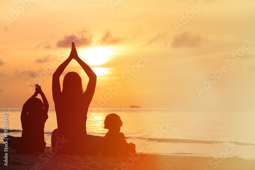 silhouette of mother and kids doing yoga at sunset