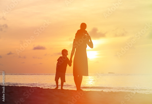mother with two kids walking on sunset beach