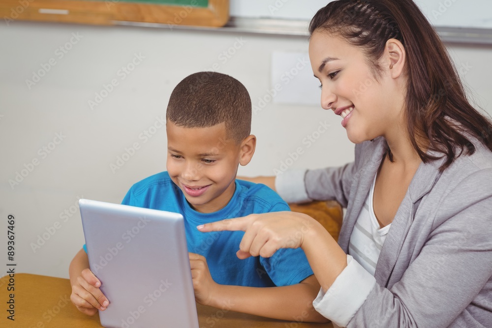 Pretty teacher and pupil using tablet at his desk Pretty teacher and pupil using tablet at his desk
