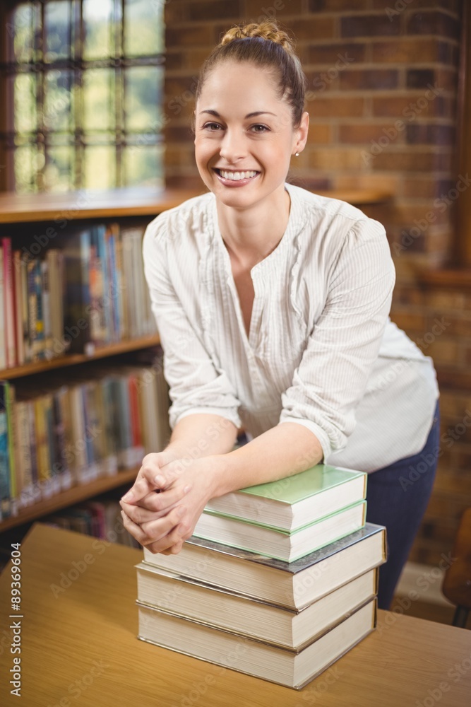 Blonde teacher leaning on pile of books in the library Blonde teacher leaning on pile of books in the library