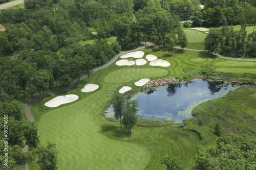 Aerial view of golf fairway and green with traps, pond and trees