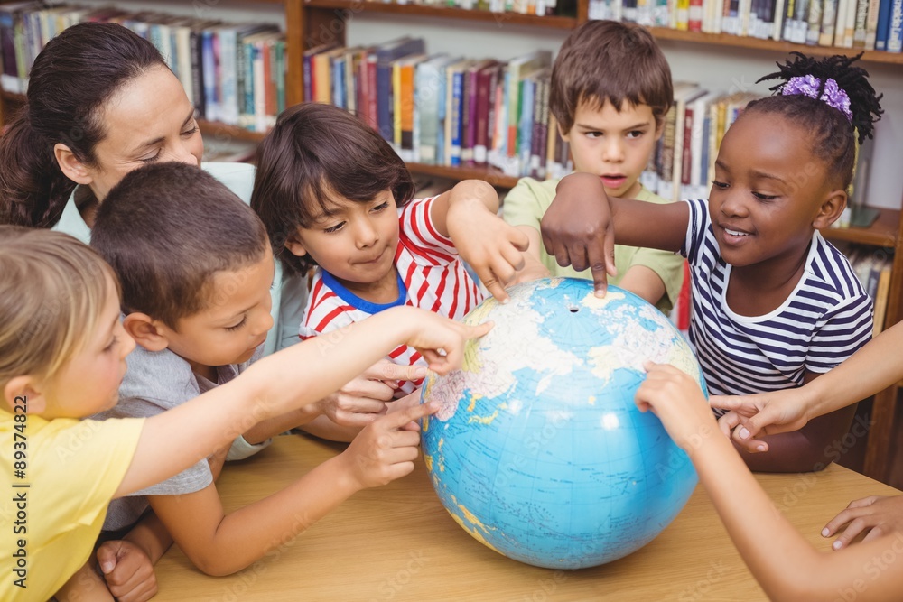 Fototapeta premium Pupils and teacher looking at globe in library