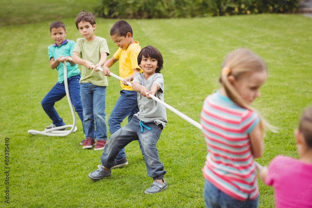 Cute pupils playing tug of war on the grass outside 