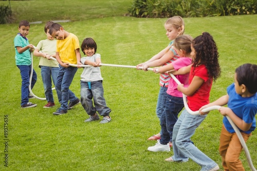 Cute pupils playing tug of war on the grass outside 