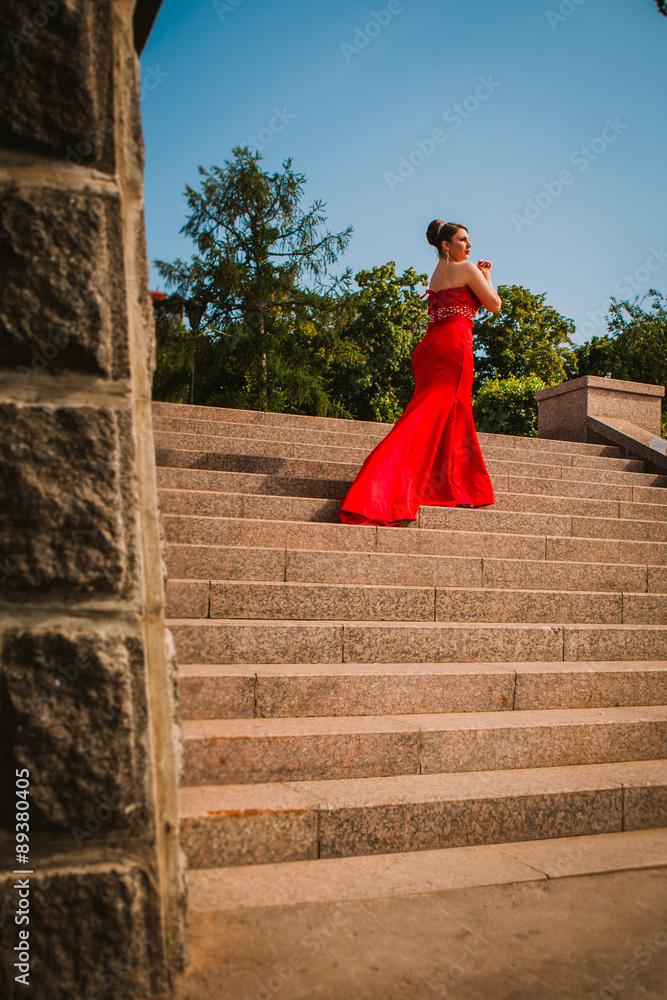 beautiful girl in a long red evening dress standing on the background of trees and shrubs beautiful girl in a long red evening dress standing on the background of trees and shrubs