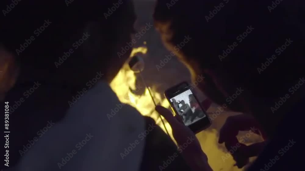 Friends look at pictures on a phone by the fire Friends look at pictures on a phone by the fire