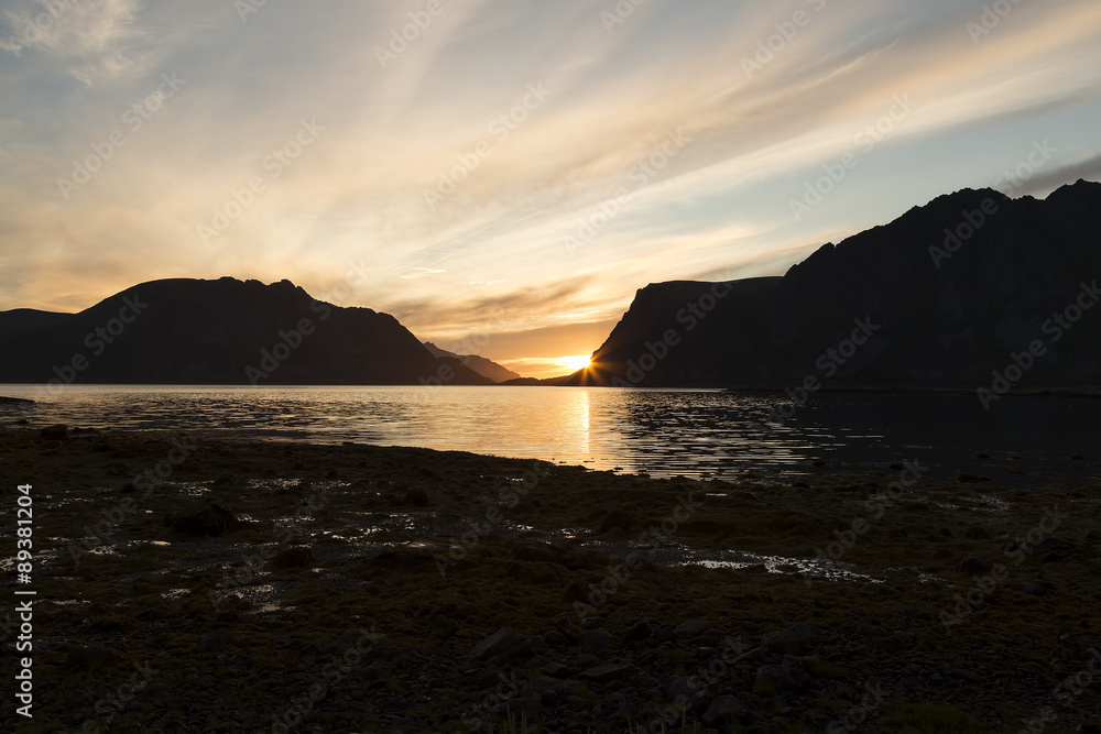 A setting sun behind some mountains in Lofoten with some water in the foreground