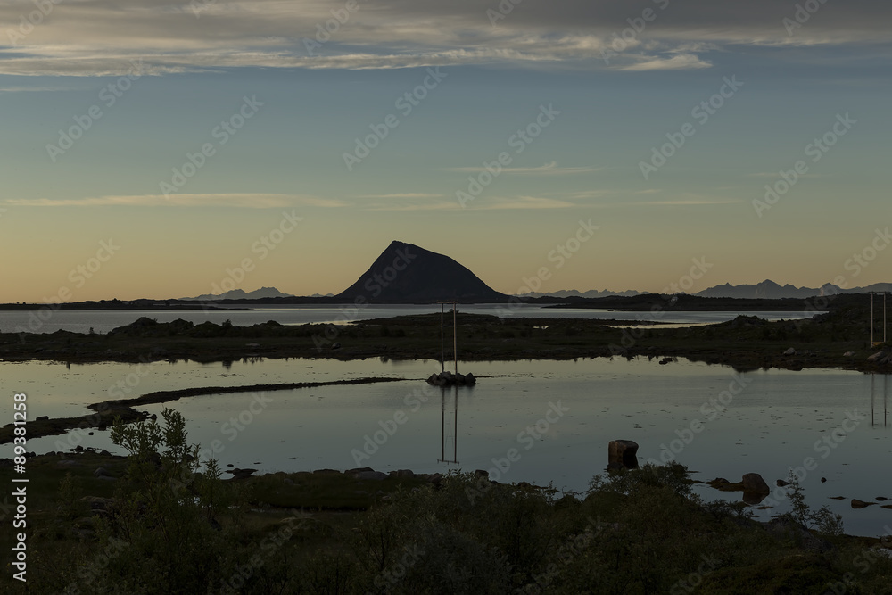 A mountain shaped like a shark fen. A power line in the foreground reflected in the water