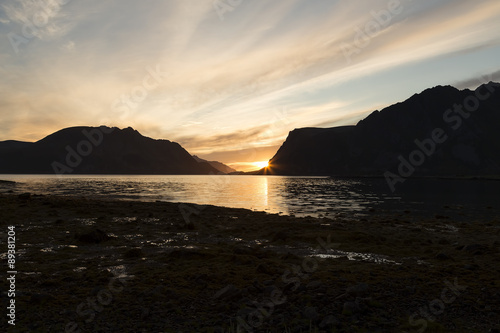 A setting sun behind some mountains in Lofoten with some water in the foreground