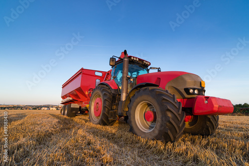 Agriculture tractor and trailer on a stubble field  copy space for text