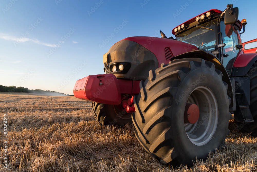 Naklejka premium Close up view of an agriculture tractor on a stubble field, soft evening ligt on a sunny day. Detail of a powerful new farming vehicle. Space copy for text