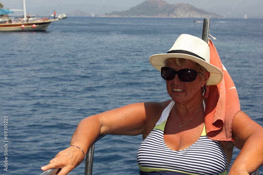 A mature woman wearing sunglasses and a hat  while on a boat trip during a vacation in turkey