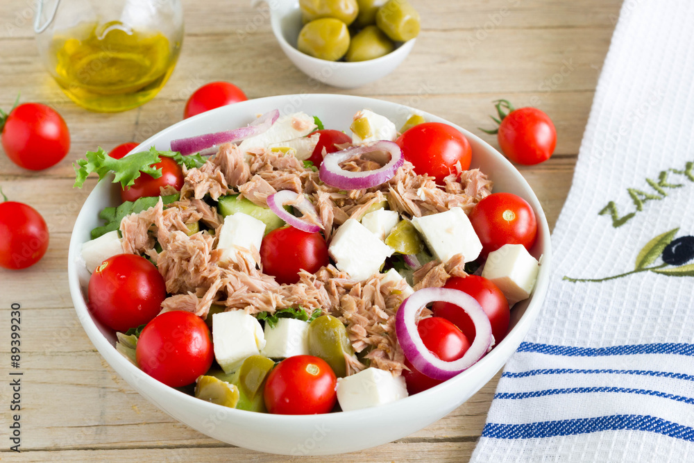 Greek salad with tuna in a white plate on a wooden table.
