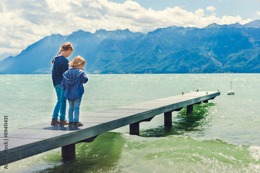 Cute kids playing by the lake, resting on a pier, wearing blue clothes, toned image