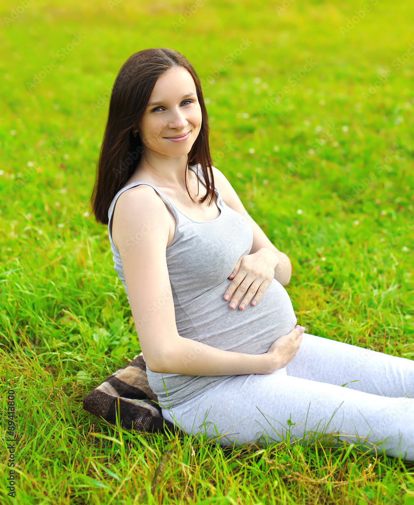 Happy smiling pregnant woman sitting on the grass in summer day Happy smiling pregnant woman sitting on the grass in summer day
