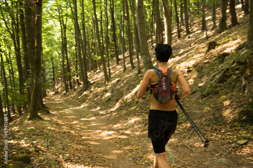 woman with backpack and poles running on the trail in the sunlit forest 