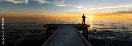 Panorama view of lonely man fishing alone during sunset at Bagan Sungai Burong Jetty with orange skies