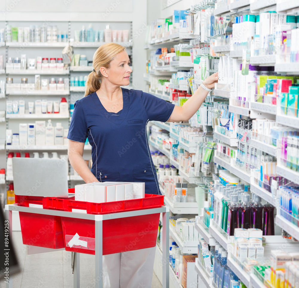 Chemist Arranging Medicines In Shelves At Pharmacy