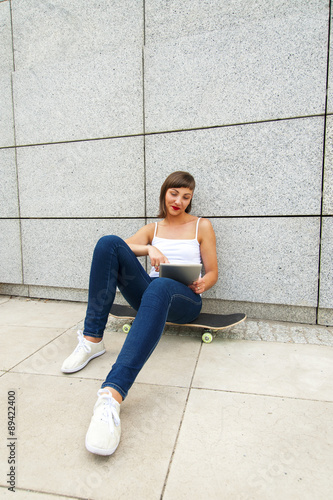 Young girl siting on skateboard in the city with tablet by the w © Wisiel