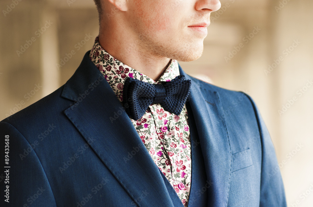 Fototapeta premium Ciemnoniebieska muszka z kwiatową koszulą i kostiumem na męskiej szyi.