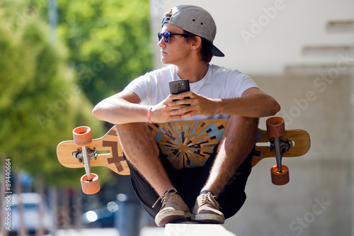 Handsome skater boy using his mobile phone in the street.