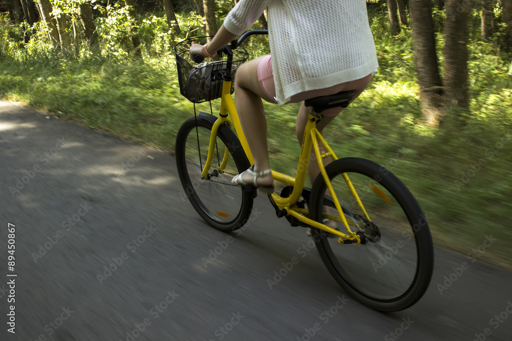 Riding yellow bicycle on the forest road. Close-up of young woman riding bicycle Riding yellow bicycle on the forest road. Close-up of young woman riding bicycle