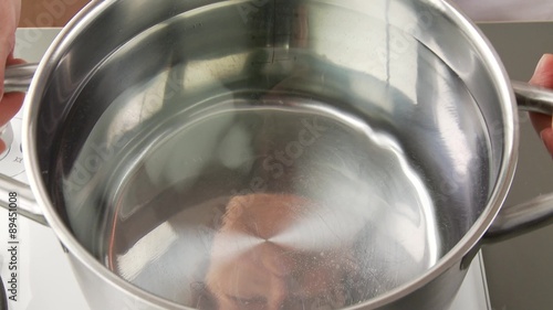A gas cooked being turned on and a pot of water being placed upon it