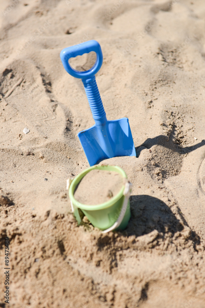a beach bucket and a beach shovel stuck in the sand by a child a beach bucket and a beach shovel stuck in the sand by a child
