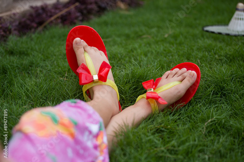 only feet of a girl wearing red slippers and sitting in grass 