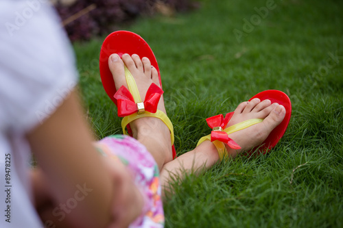 only feet of a girl wearing red slippers and sitting in grass 