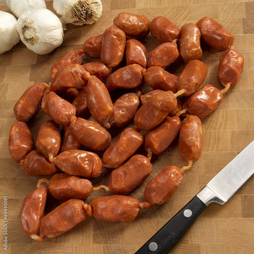 Spanish Spicy Small Link Sausages on a Cutting Board; Knife Spanish Spicy Small Link Sausages on a Cutting Board; Knife