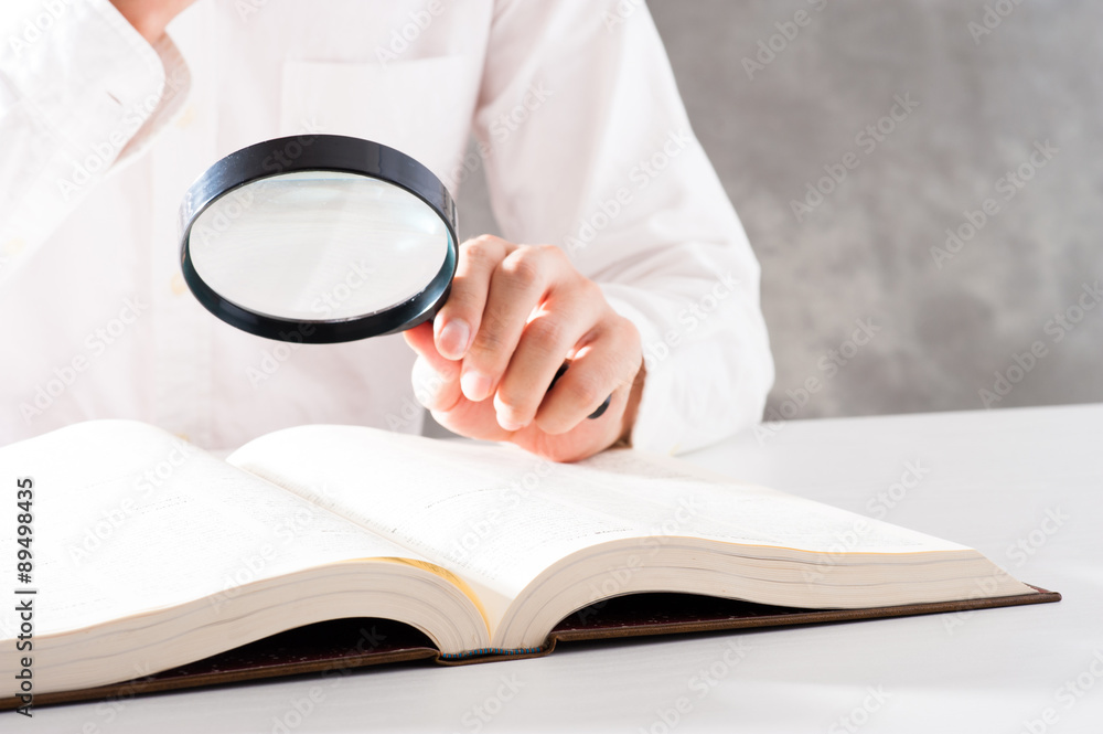 Naklejka premium 虫眼鏡を使って本を調べる男性