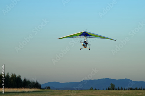 Fotografie Hang glider flying over the landscape in the early evening.