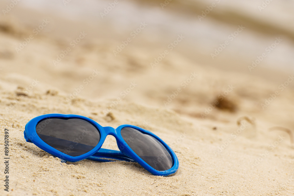 Blue sunglasses shaped heart on the sand