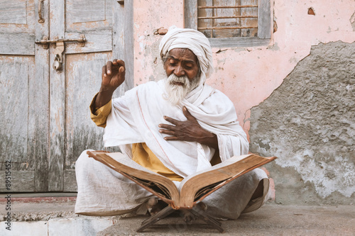 Tableau sur toile Close up of an old indian sadhu (saint) sitting and reading sacred texts near the temple