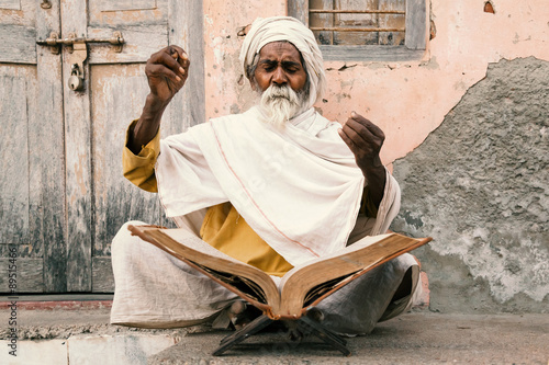 Photos Old indian sadhu (saint) sitting and speak up sacred texts with closed eyes near the temple