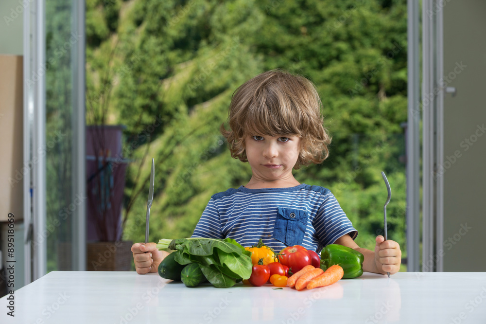 Cute little boy sitting at the table, frowning over vegetable meal, bad ...