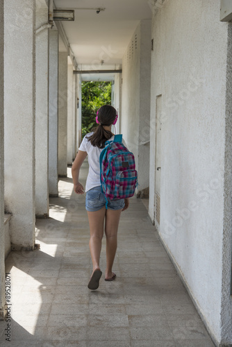 Teenage school girl with a backpack on her back and headphones. back view