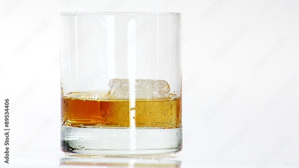 Pouring whisky into a glass with one ice cube Pouring whisky into a glass with one ice cube