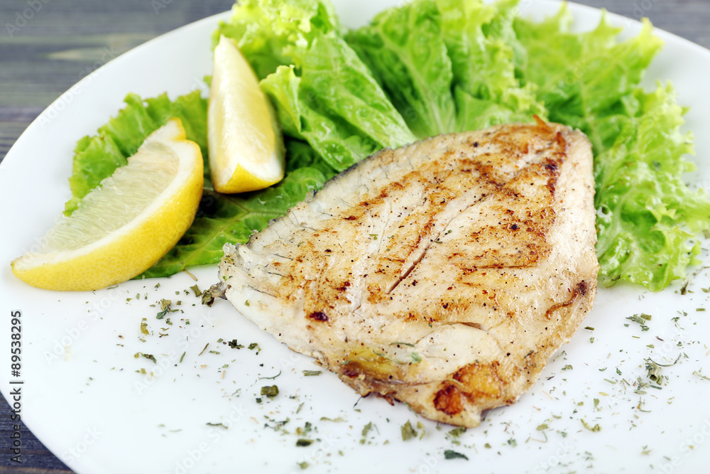 Dish of fish fillet with lettuce and lemon on table close up Dish of fish fillet with lettuce and lemon on table close up