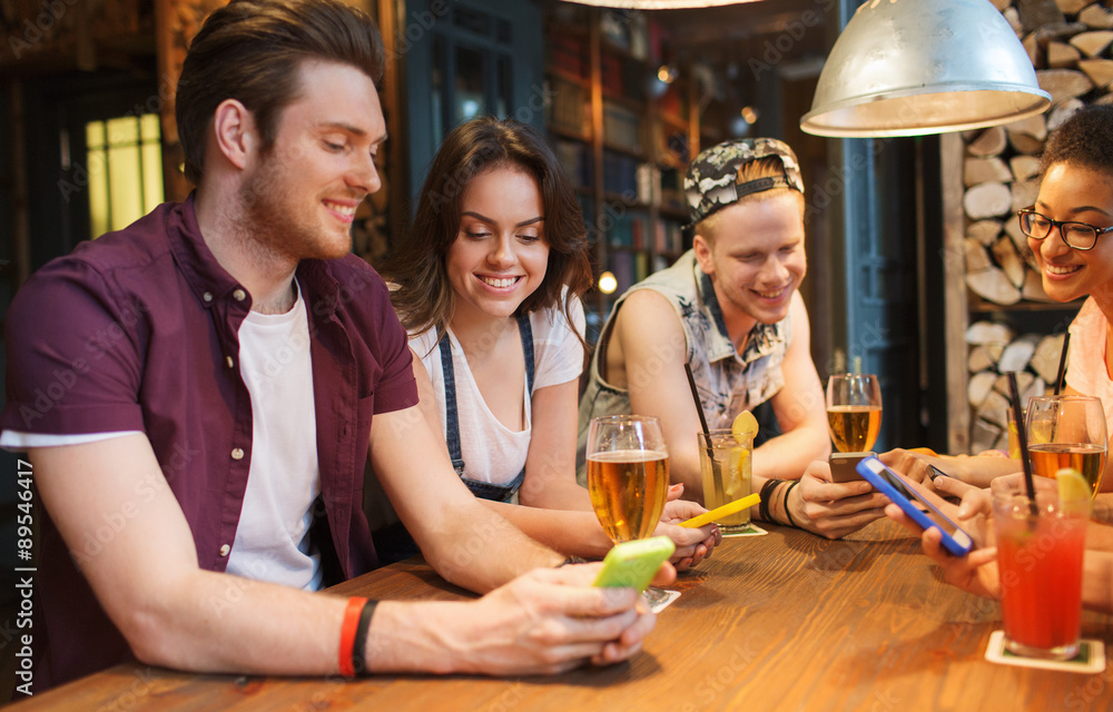 happy friends with smartphones and drinks at bar