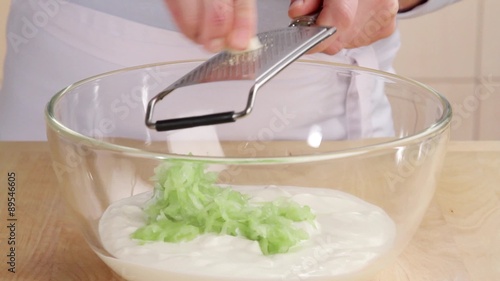 A garlic clove being grated into a cucumber and yogurt mixture