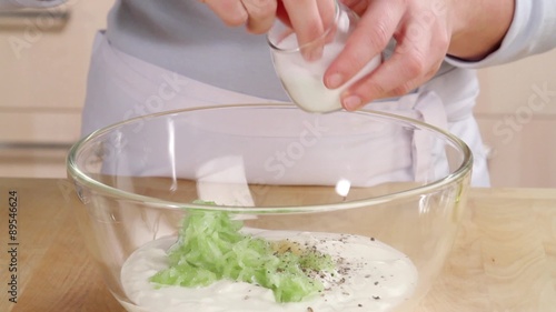 Yogurt and cucumber being seasoned with salt and drizzled with olive oil