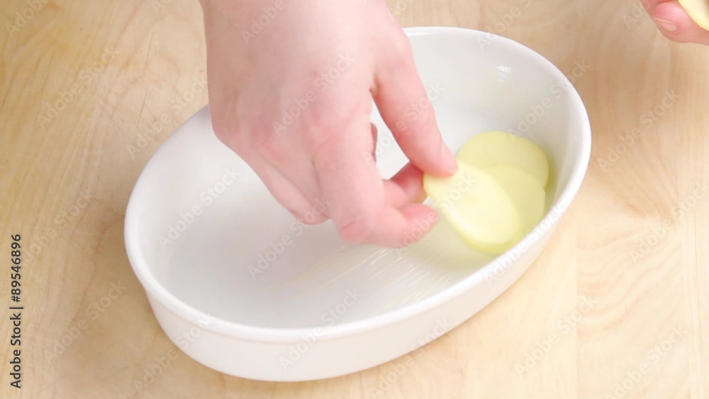 Potato slices being layered into a baking dish Potato slices being layered into a baking dish
