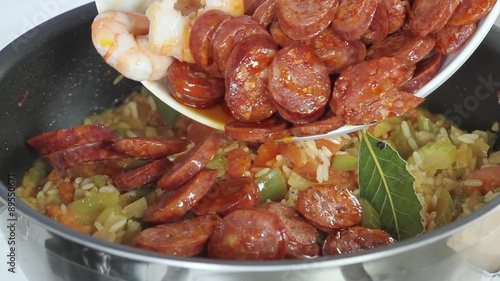 Jambalaya being made: sliced sausages and prawns being added to a rice and vegetable stew