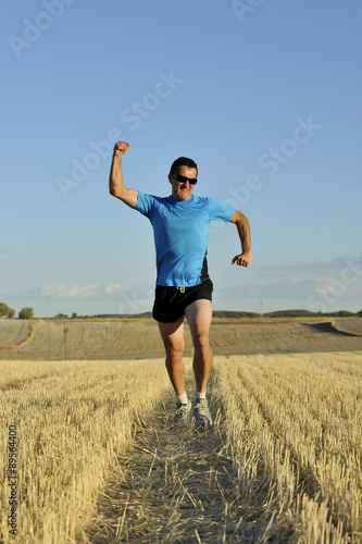 sport man running outdoors on straw field doing victory sign in frontal perspective