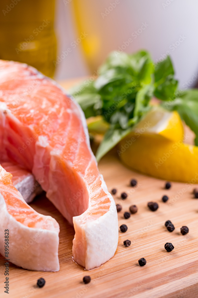 Close up on raw steak of salmon with lemon and herbs on wooden cutting board.