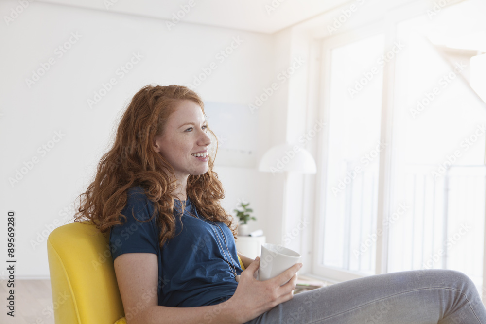 Happy young woman with cup of coffee sitting in her living room Happy young woman with cup of coffee sitting in her living room